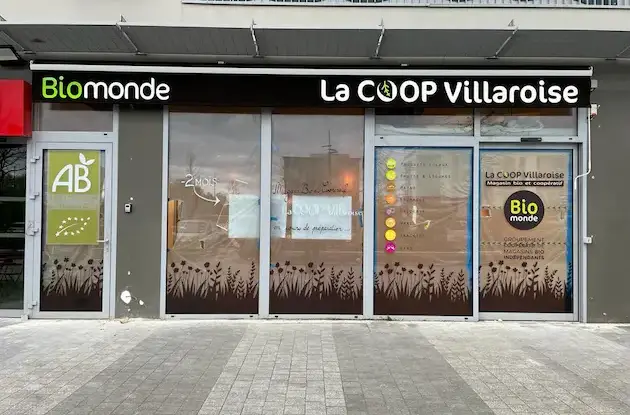Façade de magasin Biocoop avec enseigne noire et vitrophanie décorative de plantes et herbes sauvages.