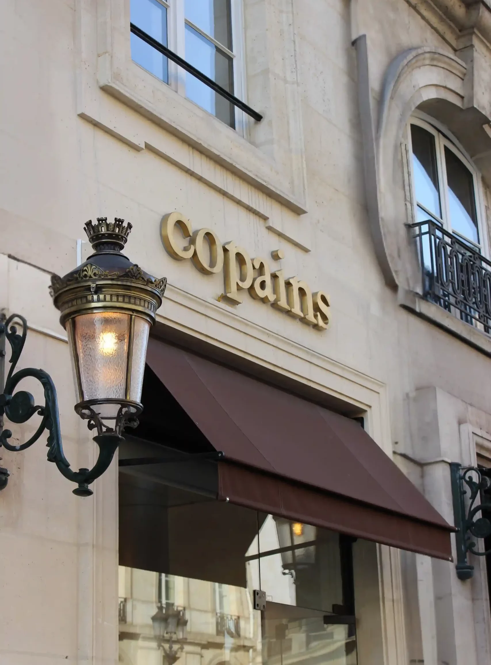 lettres découpées Copains avec lettres dorées sur une façade en pierre avec un store bannette en bas de l'enseigne