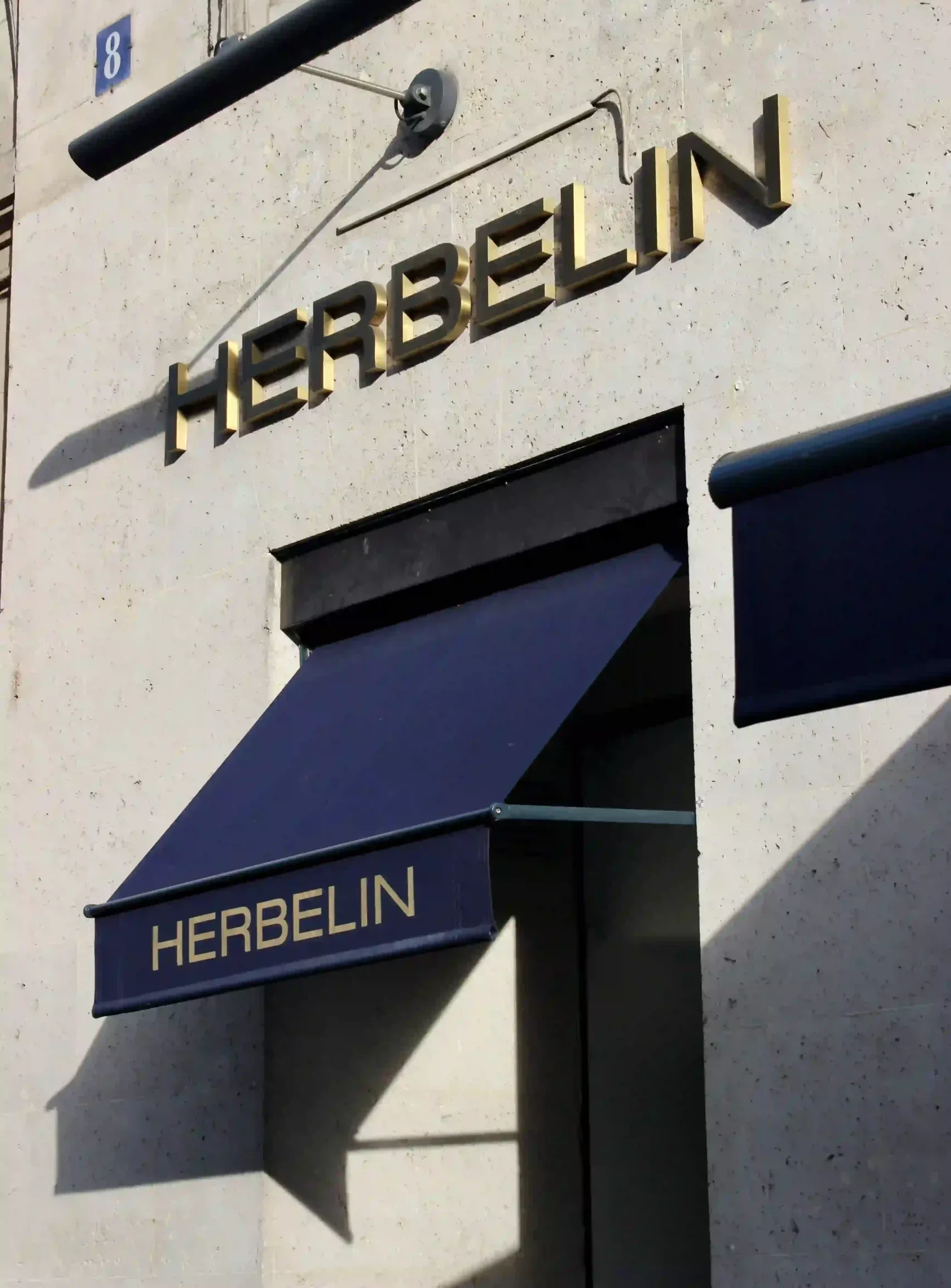 Enseigne Herbelin en lettres découpées dorées avec store banne bleu nuit fixée sur une façade claire
